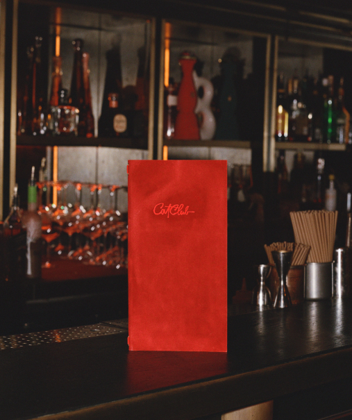 Carte de cocktails rouge Cat Club posée debout sur le comptoir du bar, bouteilles et verres en fond – cocktail courchevel