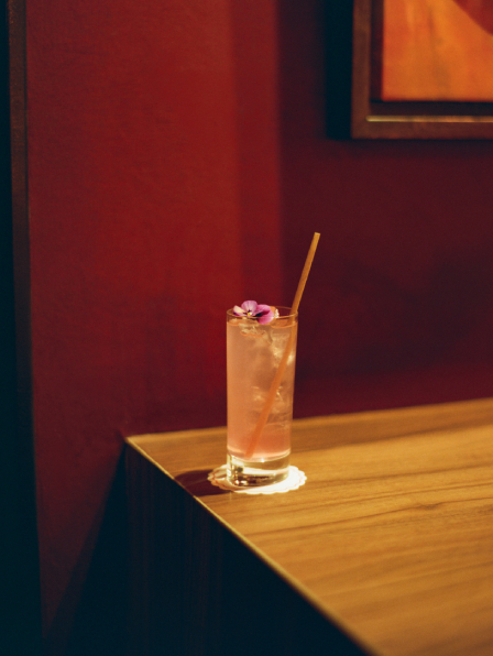 Cocktail ros&eacute; avec fleur et paille sur coin de table en bois, mur bordeaux en fond &ndash; bar courchevel
