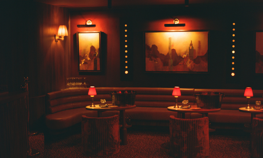 Salle lounge du Cat Club en demi-lune avec banquette cuir, tables rondes, lampes rouges et tableaux &eacute;clair&eacute;s &ndash; club courchevel
