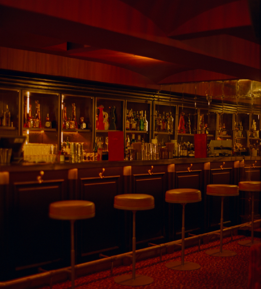 Long comptoir du bar Cat Club Courchevel avec rangée de tabourets en cuir caramel, miroirs et étagères de bouteilles rétroéclairées – bar courchevel