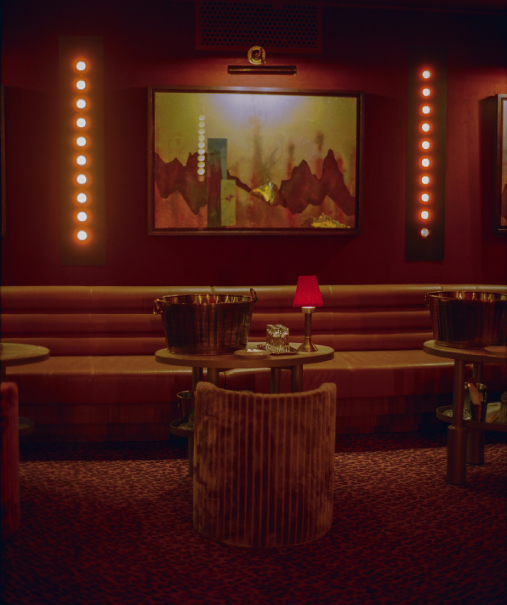 Banquette cuir rouge du Cat Club Courchevel avec seau à champagne, lampe rouge et tableau encadré sous spots – lounge courchevel