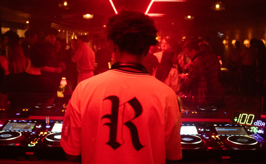 DJ de dos aux platines sous lumi&egrave;res rouges n&eacute;on avec foule en fond &ndash; soir&eacute;e Cat Club Courchevel