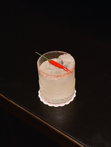 Cocktail signature en verre rocks avec piment rouge et bord givr&eacute; pos&eacute; sur comptoir noir &ndash; cocktail Cat Club Courchevel