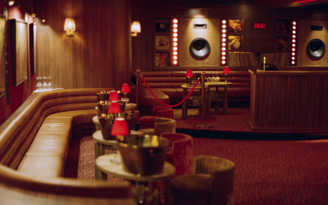 Vue d'ensemble de la salle du Cat Club avec banquettes cuir, tables rondes, lampes rouges, scène DJ et corde velours – Cat Club Courchevel