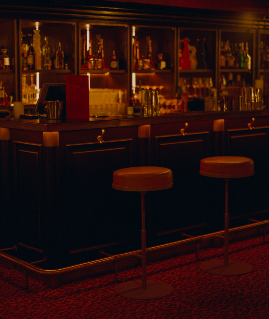 Comptoir du bar Cat Club Courchevel avec tabourets en cuir caramel et étagères de bouteilles rétroéclairées en fond sombre – bar courchevel