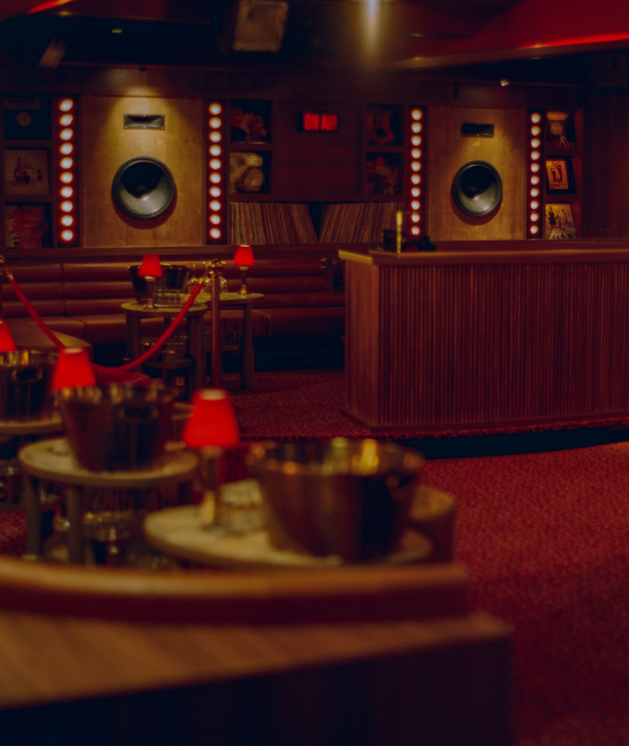 Salle du Cat Club Courchevel avec enceintes sur scène, panneau ON AIR, banquettes cuir et tables rondes aux lampes rouges – club courchevel
