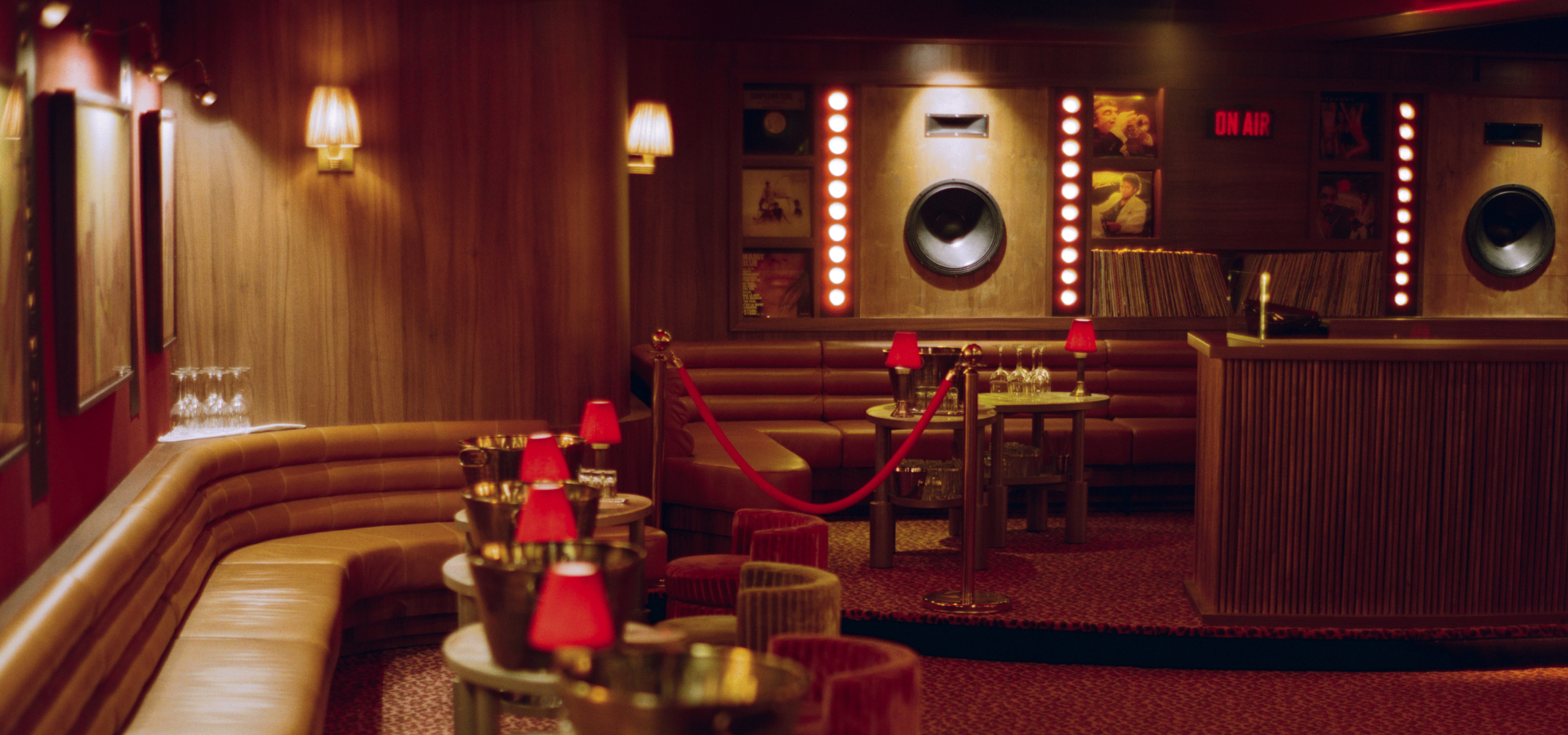 Salle lounge du Cat Club Courchevel avec banquettes cuir, tables rondes, lampes rouges et cabine DJ en fond – bar club courchevel